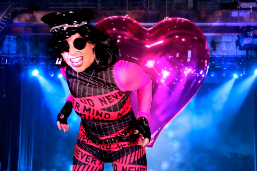 Cobra X is dancing in front of a big pink heart of glass